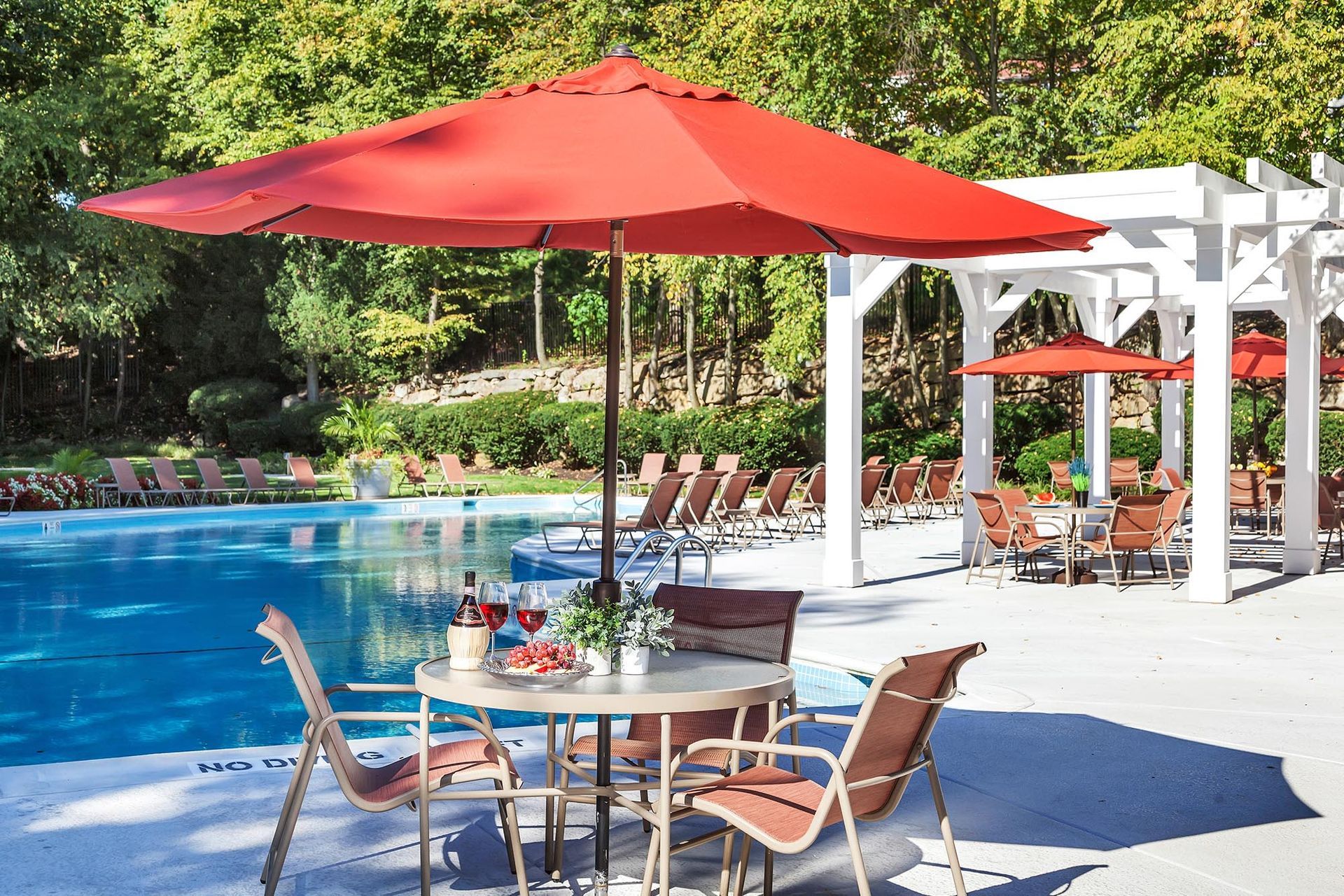 Outdoor pool area with lounge chairs, red umbrellas, and table seating.