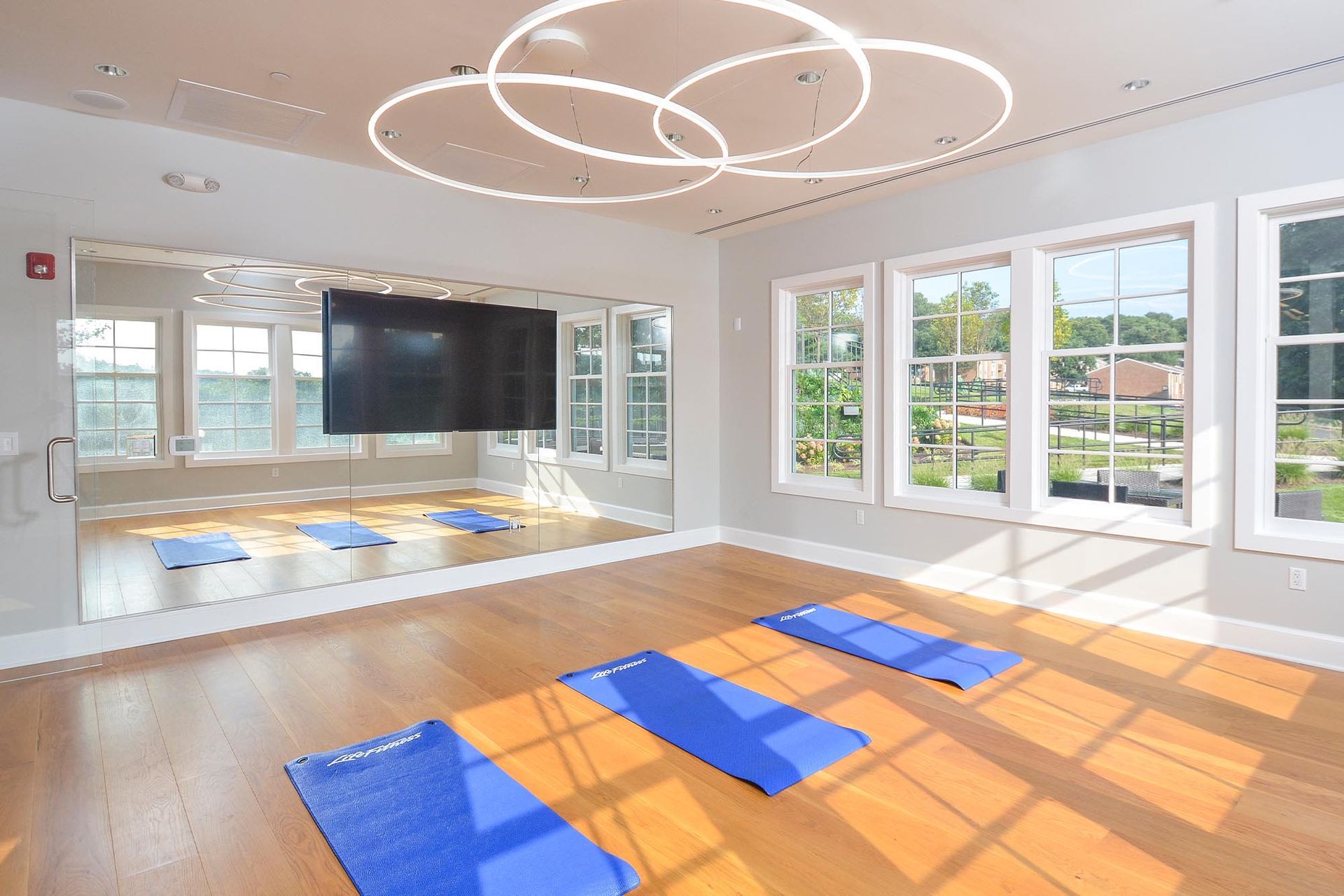 Yoga studio with blue mats on a wooden floor, mirrored wall, and circular ceiling lights.