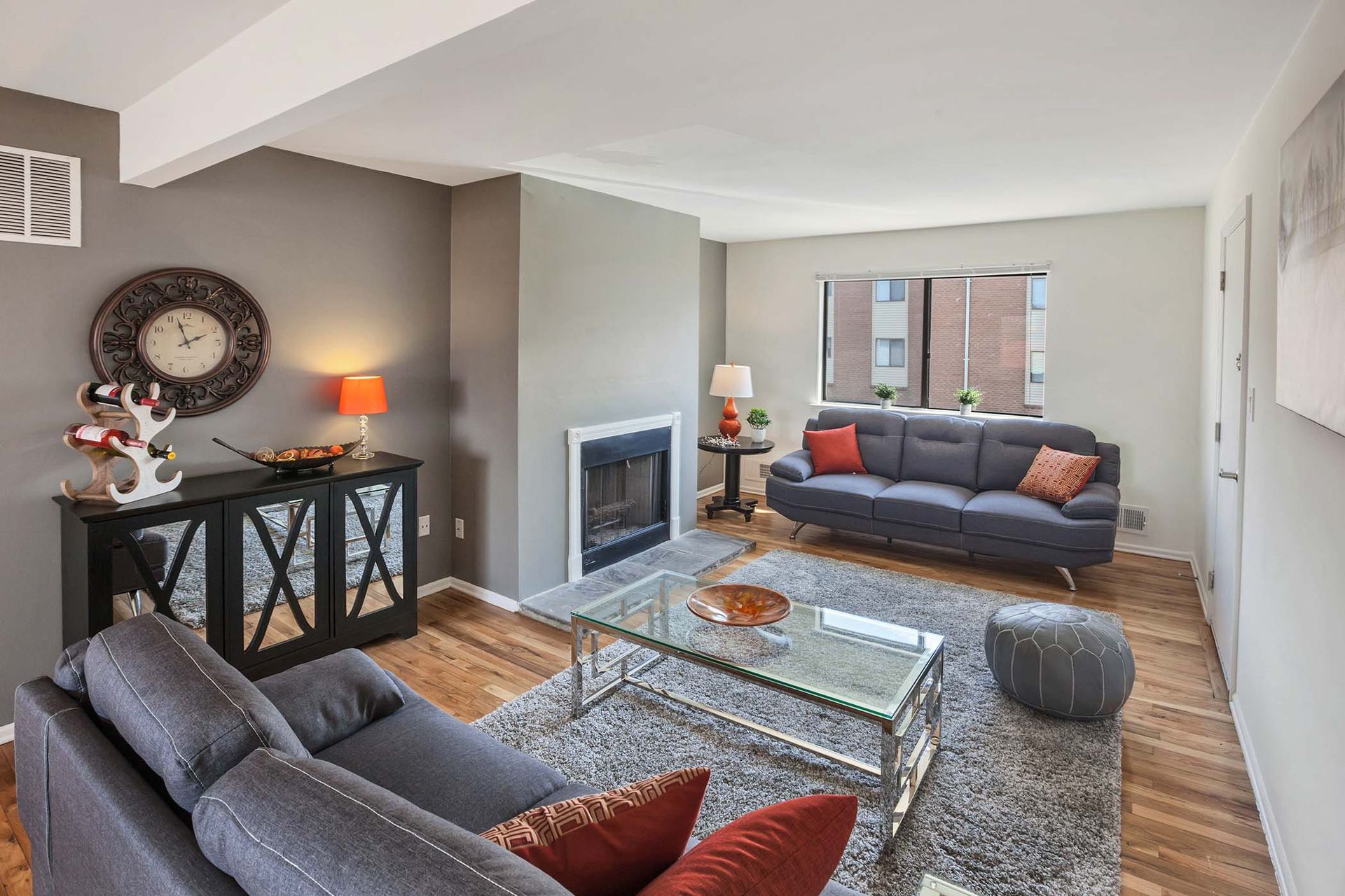 Living room in an apartment with a gray sectional sofa, glass coffee table, and a fireplace.