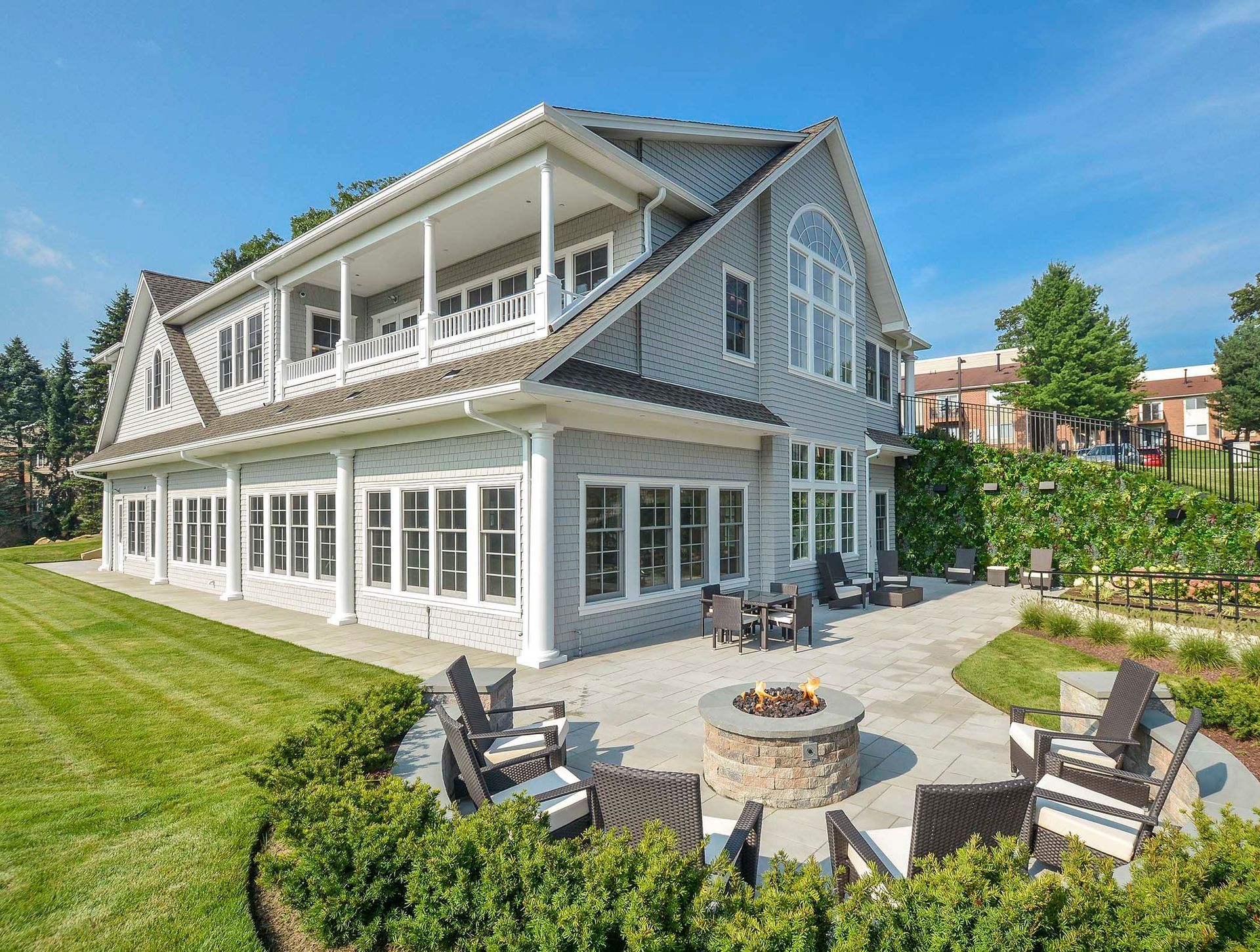 Gray house with white trim, patio with fire pit and chairs, green lawn, clear blue sky.