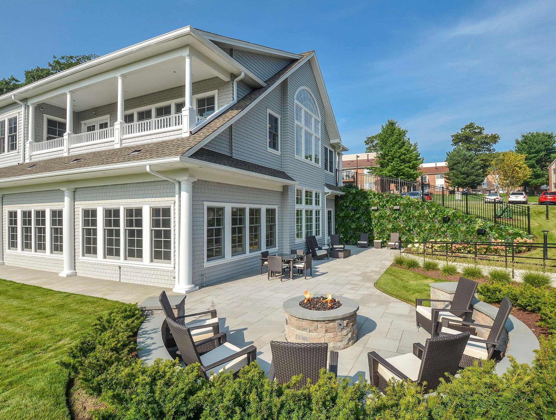 Exterior view of a two-story apartment building with a large patio, seating, and a fire pit.
