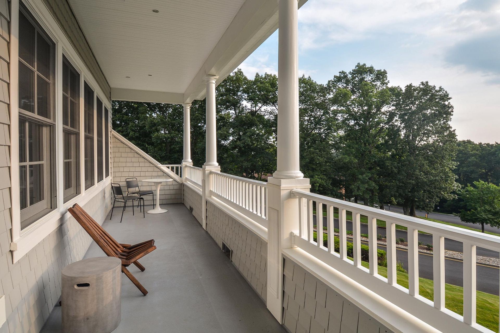 Balcony with white railings, chairs, and a small round table overlooking trees.