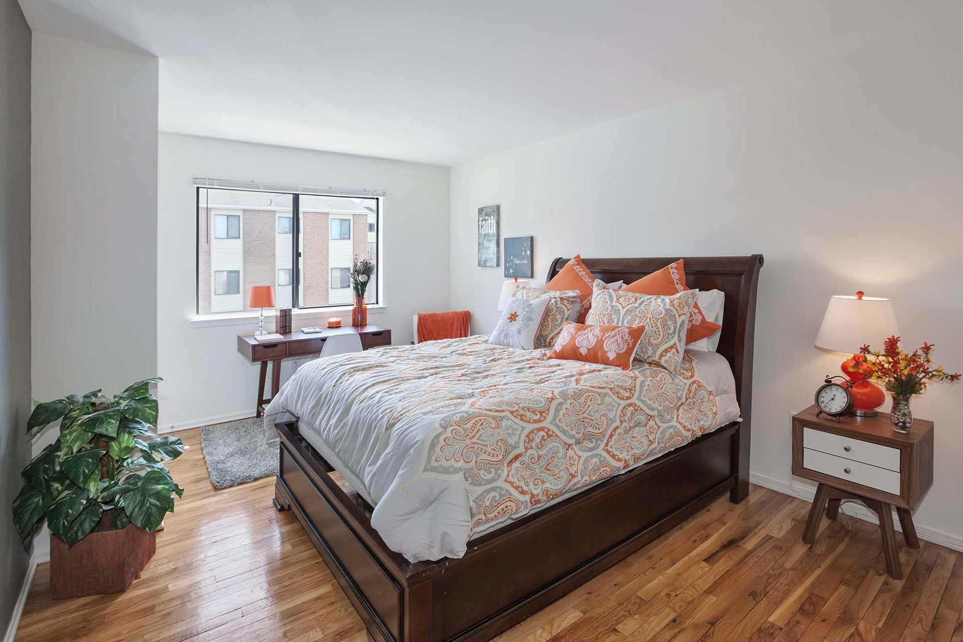 Bedroom in an apartment with a dark wooden bed, two nightstands, and a desk by a large window.