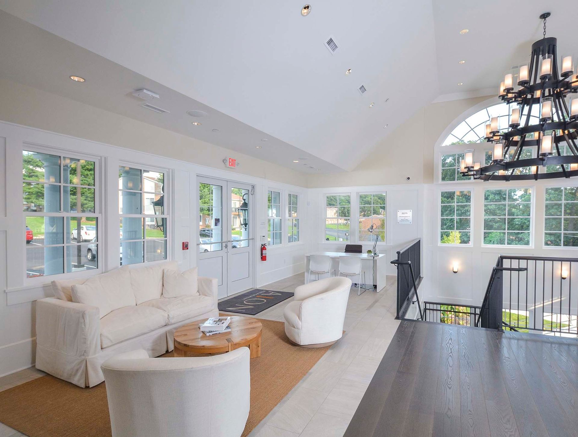 Bright communal leasing lounge with white sofas, large windows, and a black chandelier.
