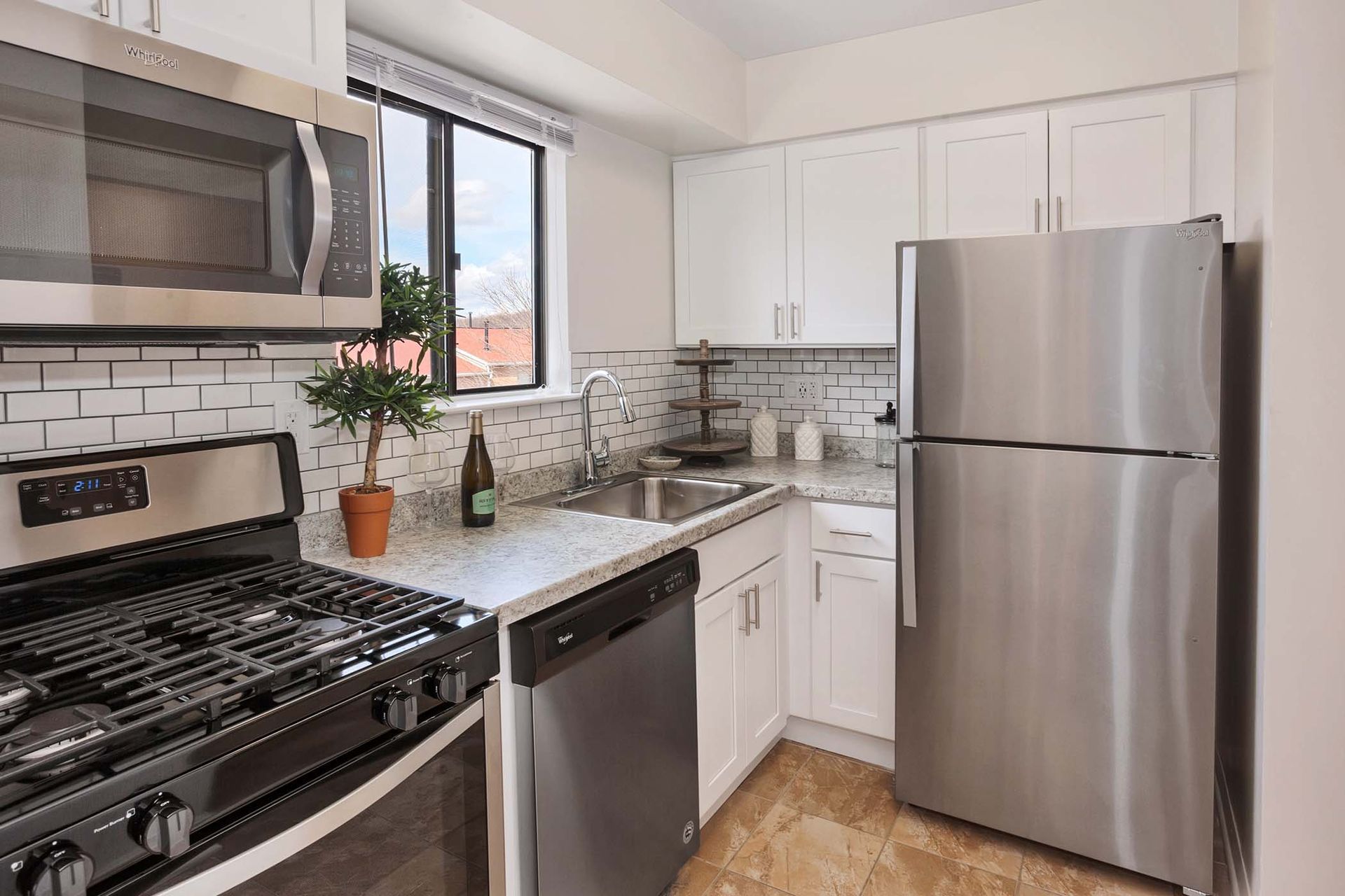 Kitchen in a modern apartment with stainless steel fridge, stove, microwave, white cabinets, and a window.