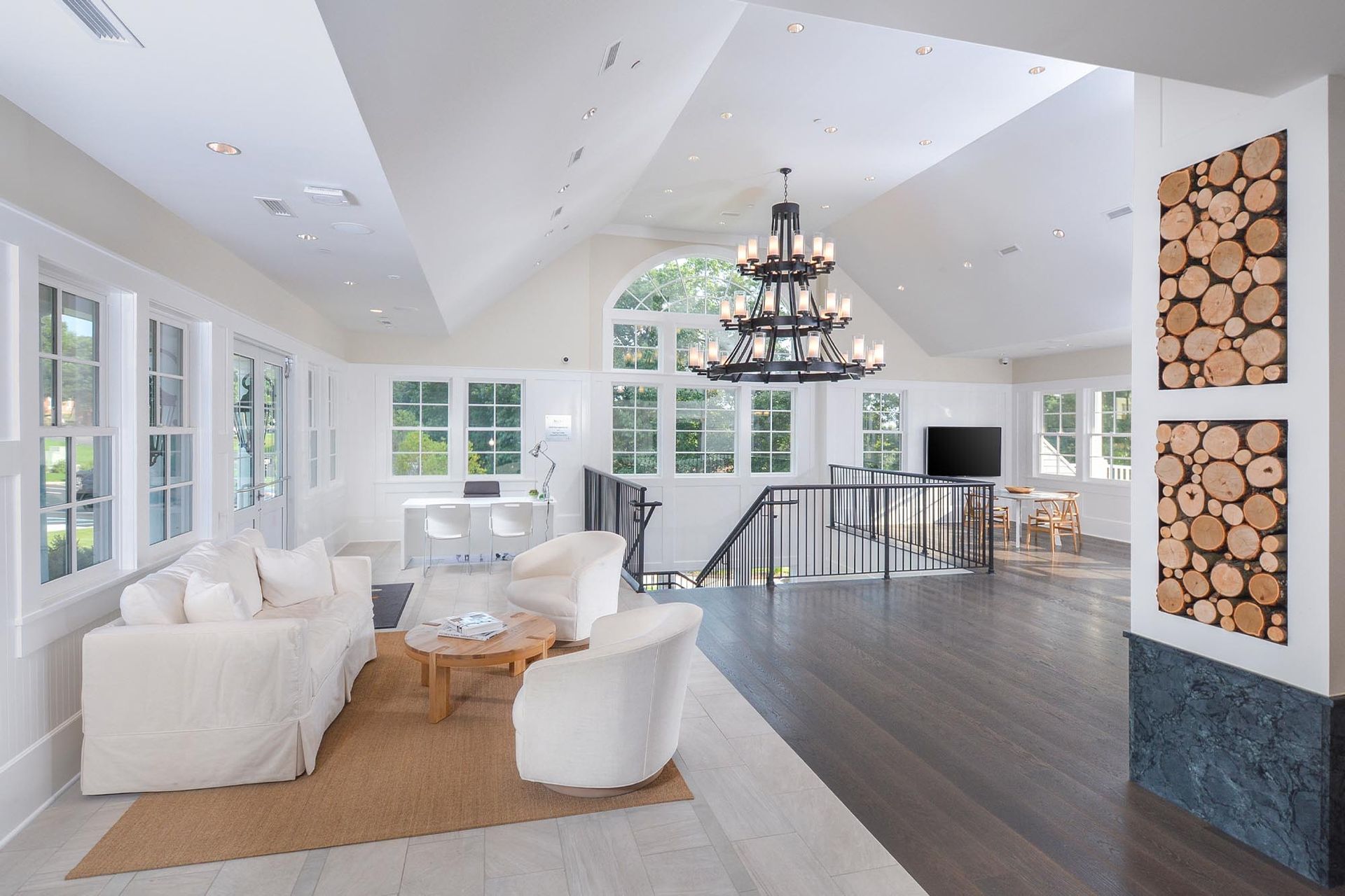 Bright communal lounge with white seating, large windows, and a central chandelier.