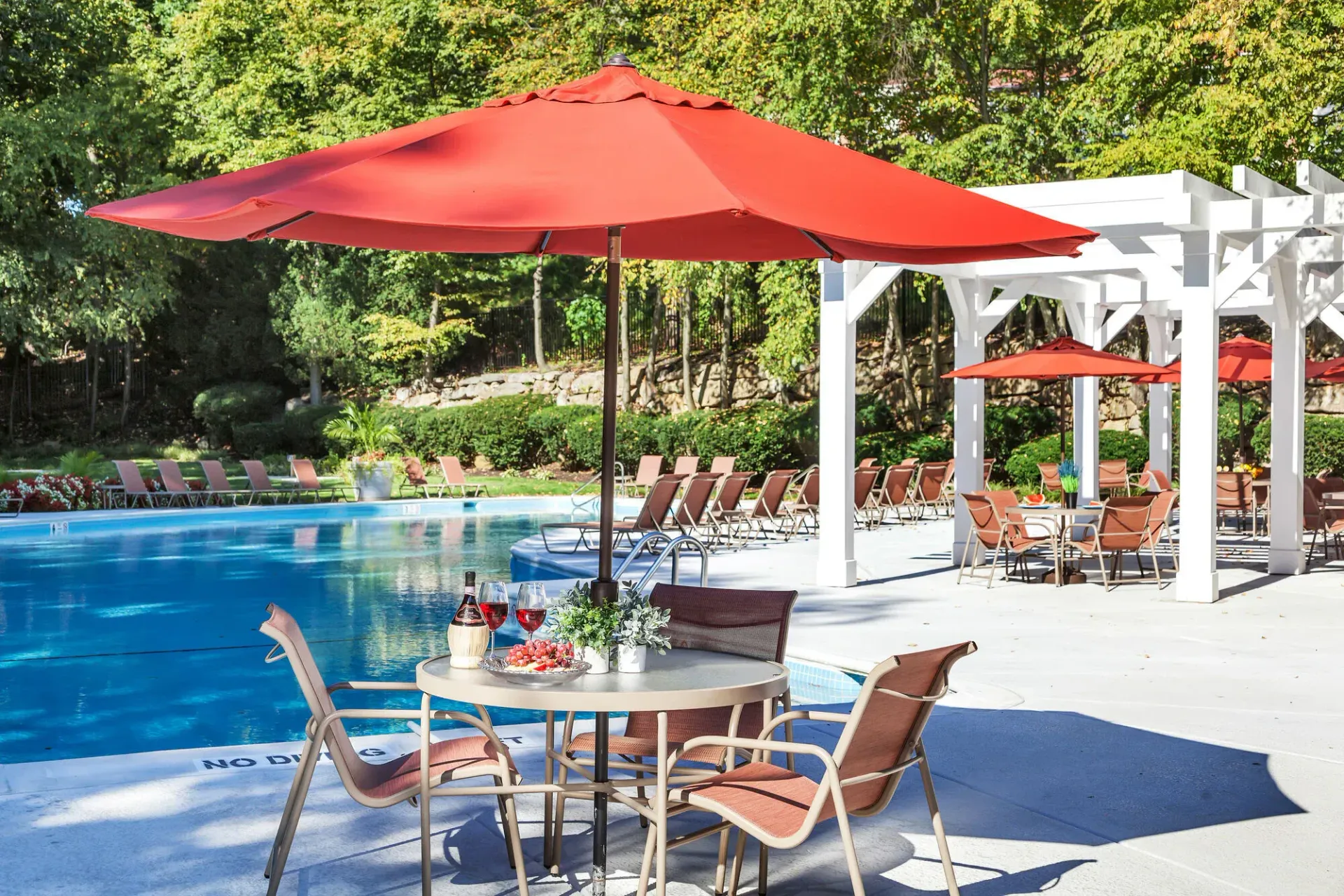 Poolside patio with red umbrella, table set for dining, and pool in background.