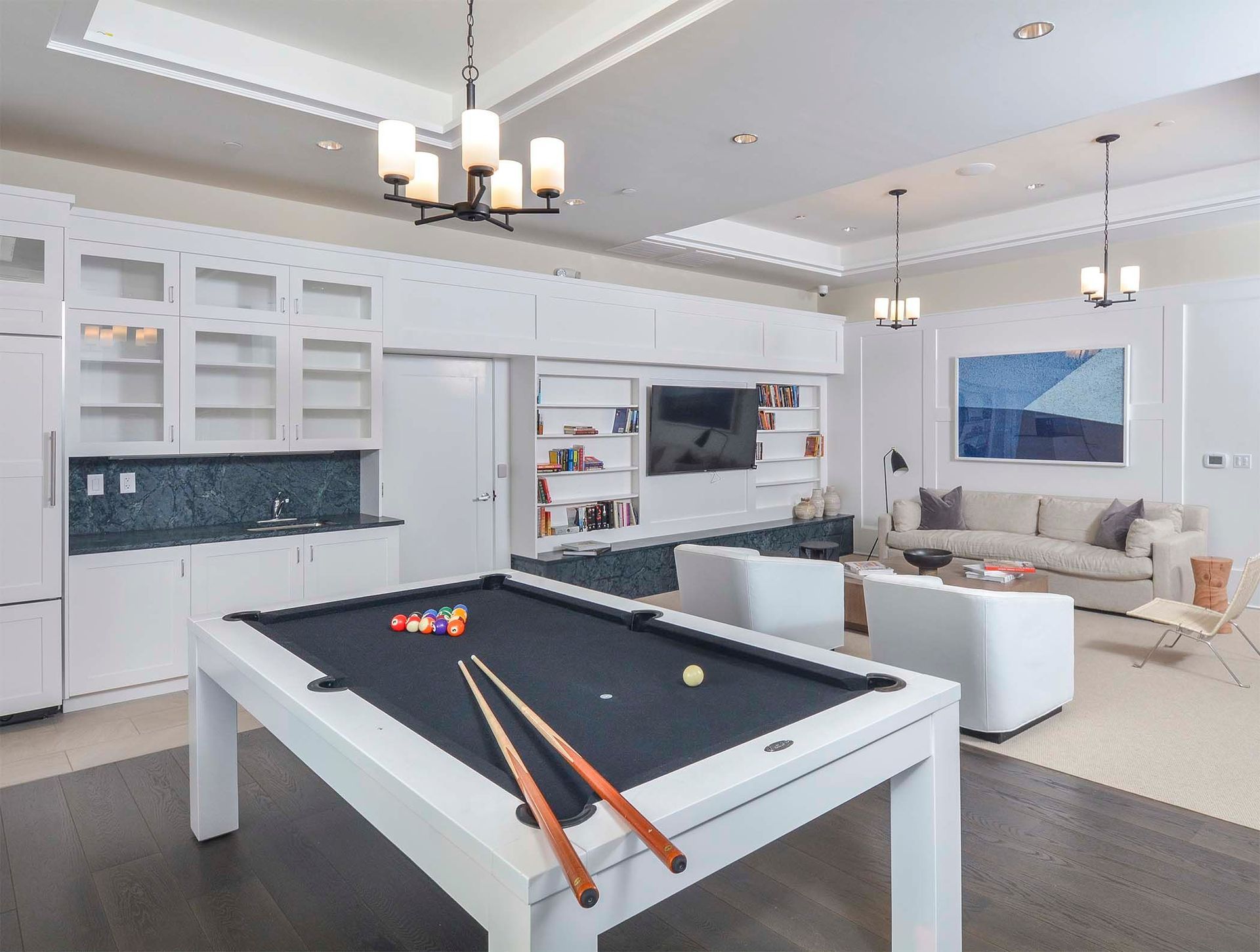 Bright communal recreation room with a white pool table, built-in white cabinets, bookshelves, TV, and a seating area.