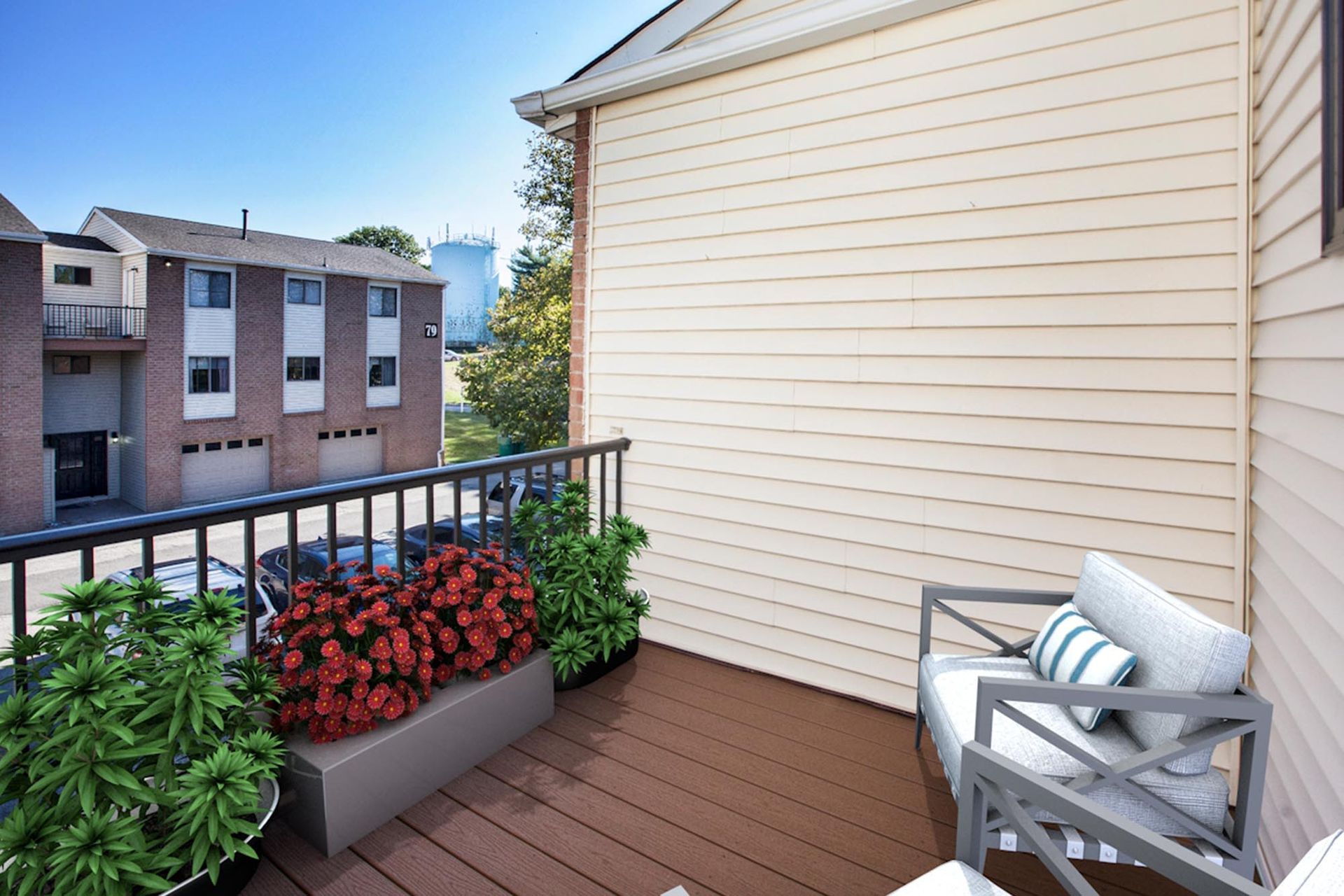Balcony with a metal-framed chair, planter boxes, beige siding, overlooking a brick apartment building.