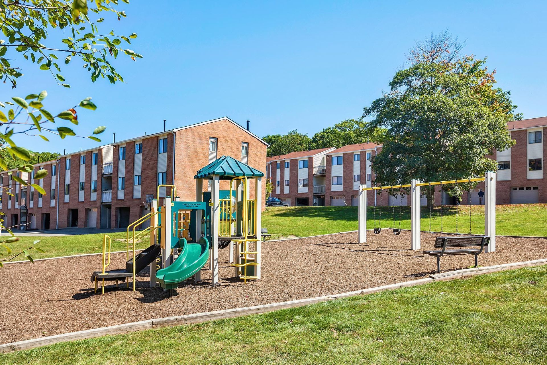 Playground with slide, swings, and seating in a grassy apartment community courtyard.