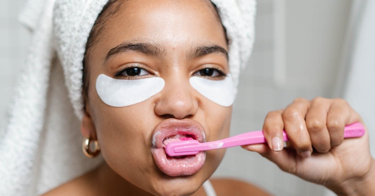 A woman with a towel wrapped around her head is brushing her teeth with a pink toothbrush.