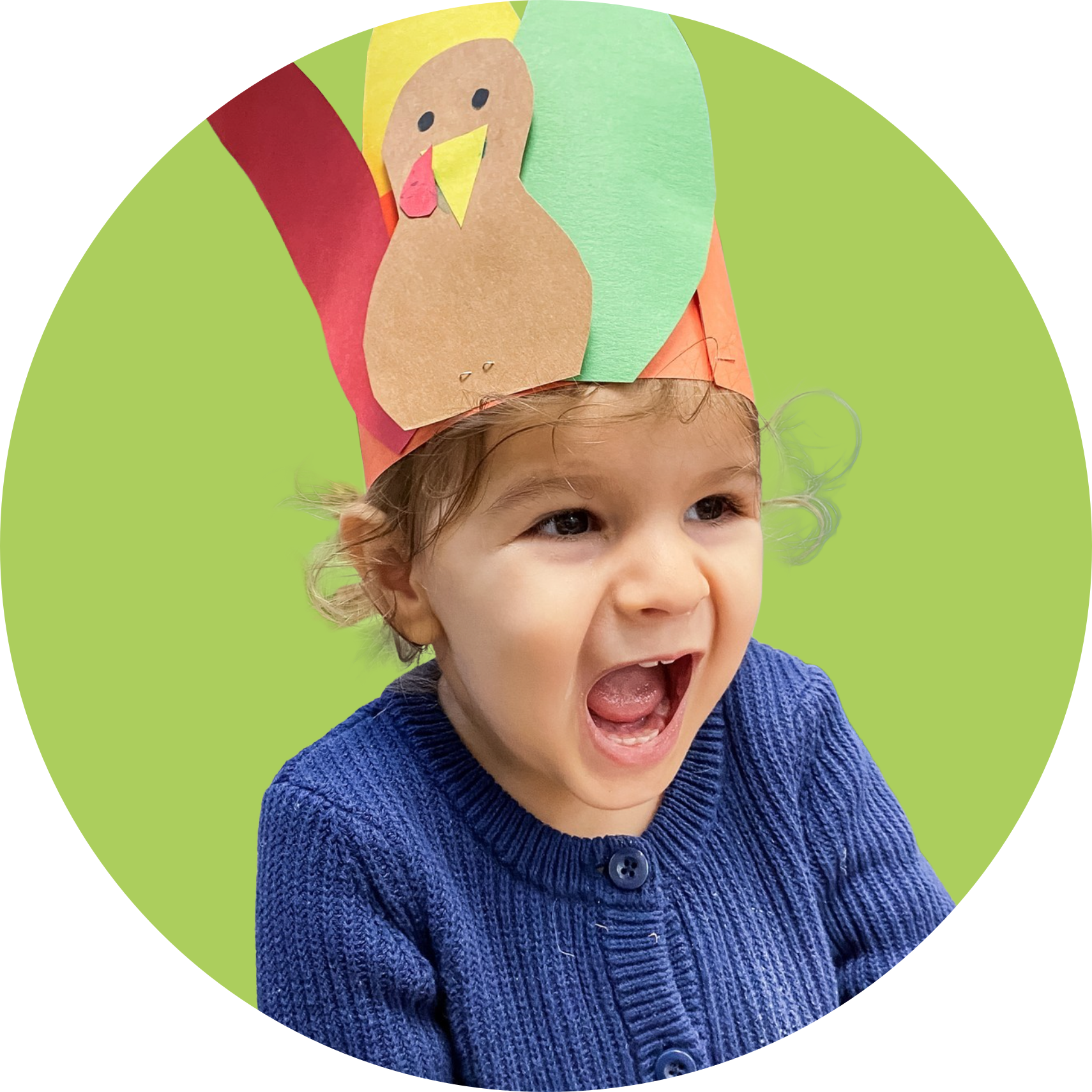Child wearing a paper turkey hat, smiling widely. Set against a green background.