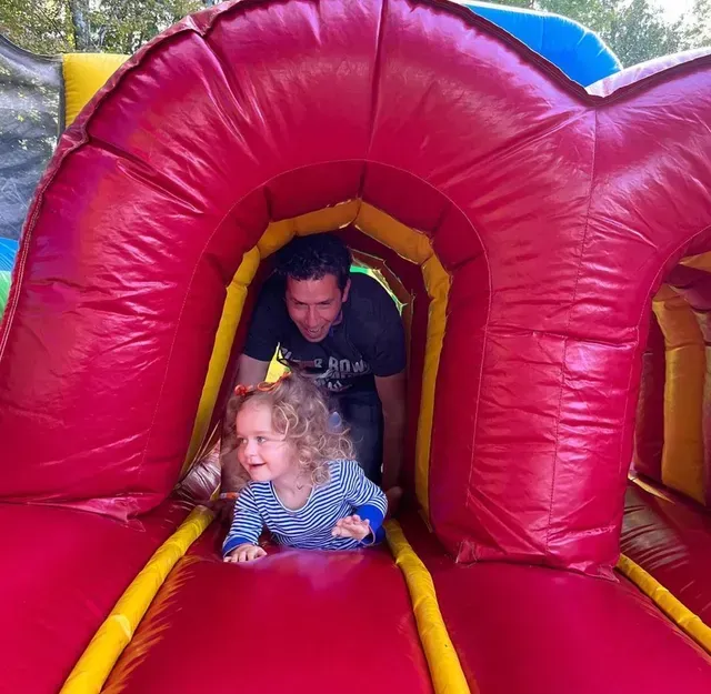 Man and child crawling through a red inflatable tunnel, smiling.