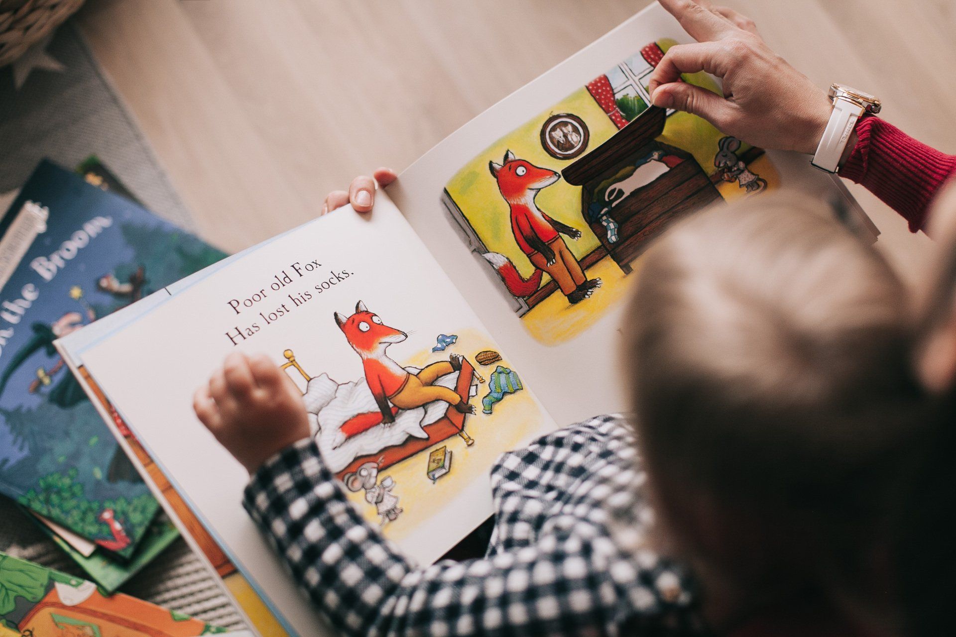 Child looking at a colorful open book with a fox illustration, held by an adult.