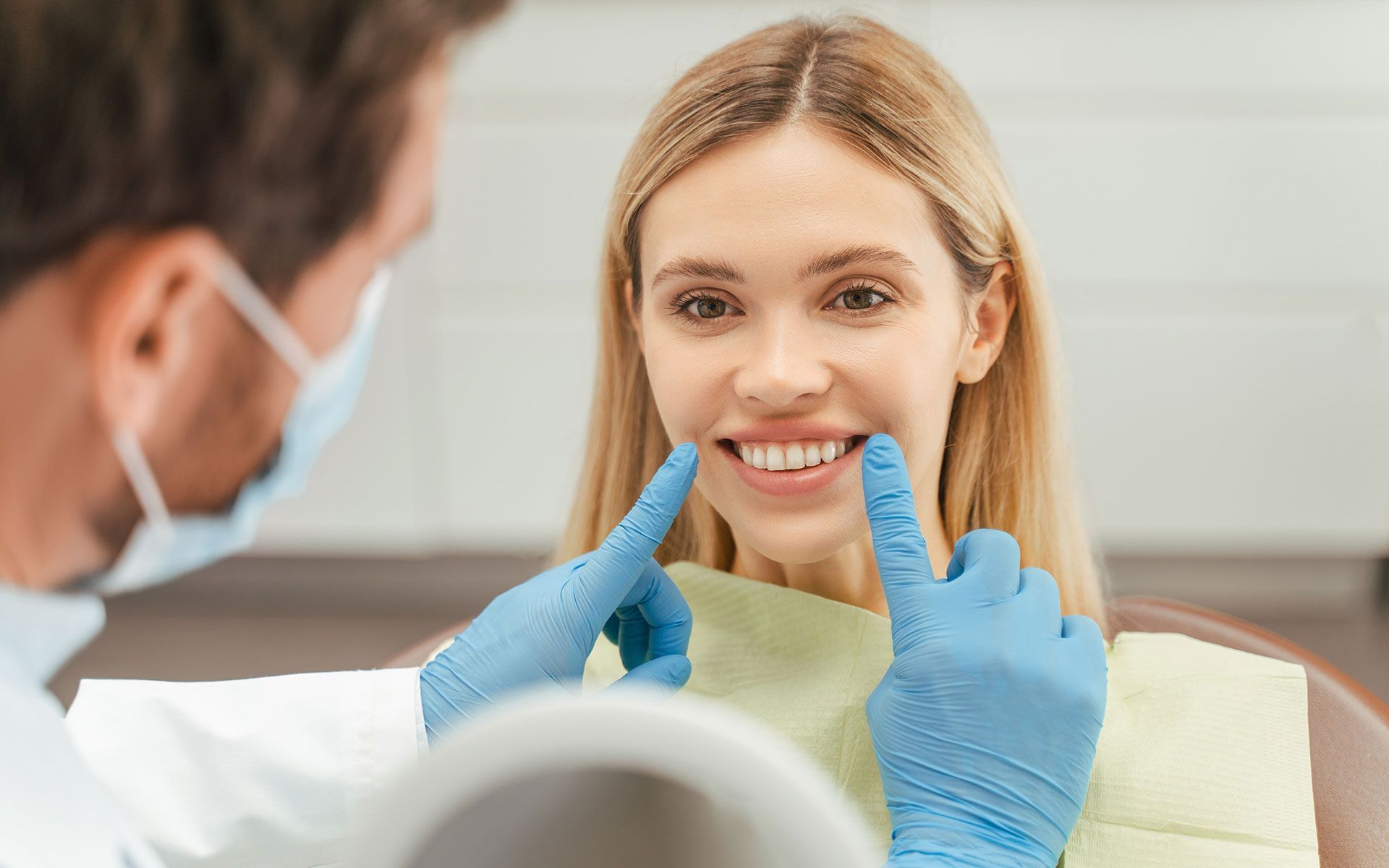 A woman is sitting in a dental chair while a dentist examines her teeth.
