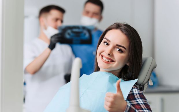 A woman is giving a thumbs up while sitting in a dental chair.