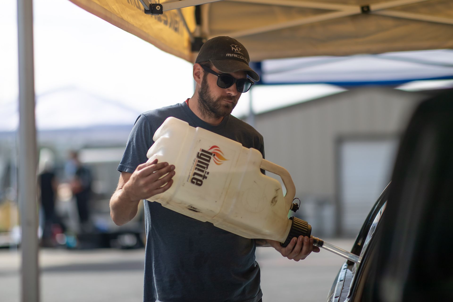A man is pouring gas into a car under a tent.
