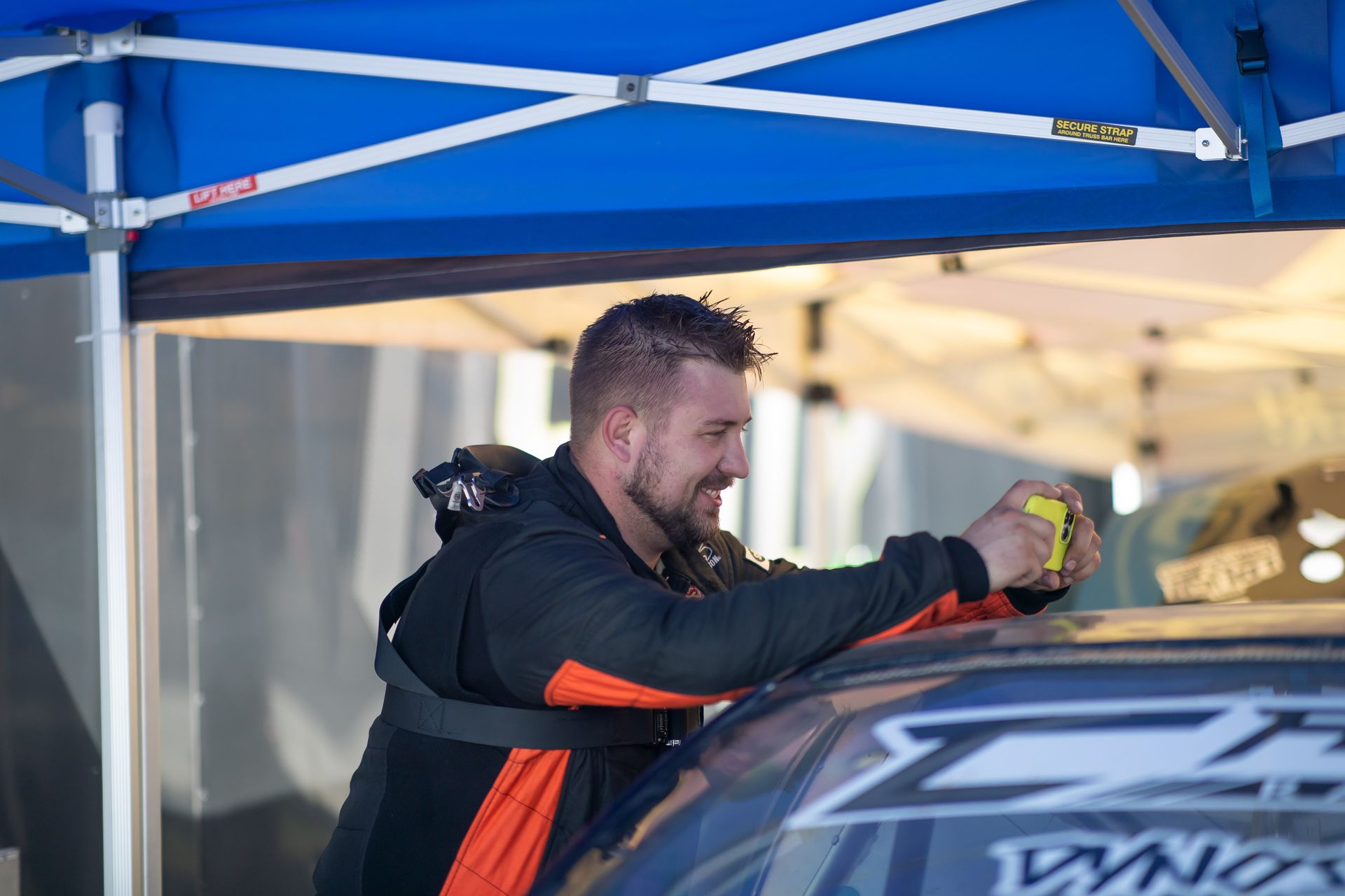 A man is cleaning the roof of a car under a blue tent.