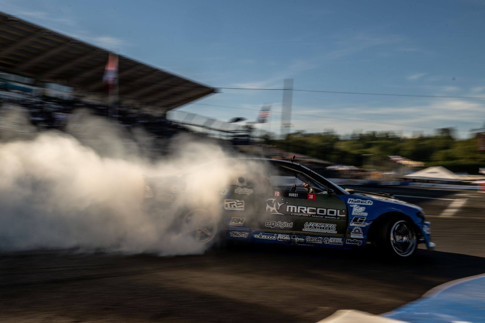A blue car is doing a burnout on a race track.