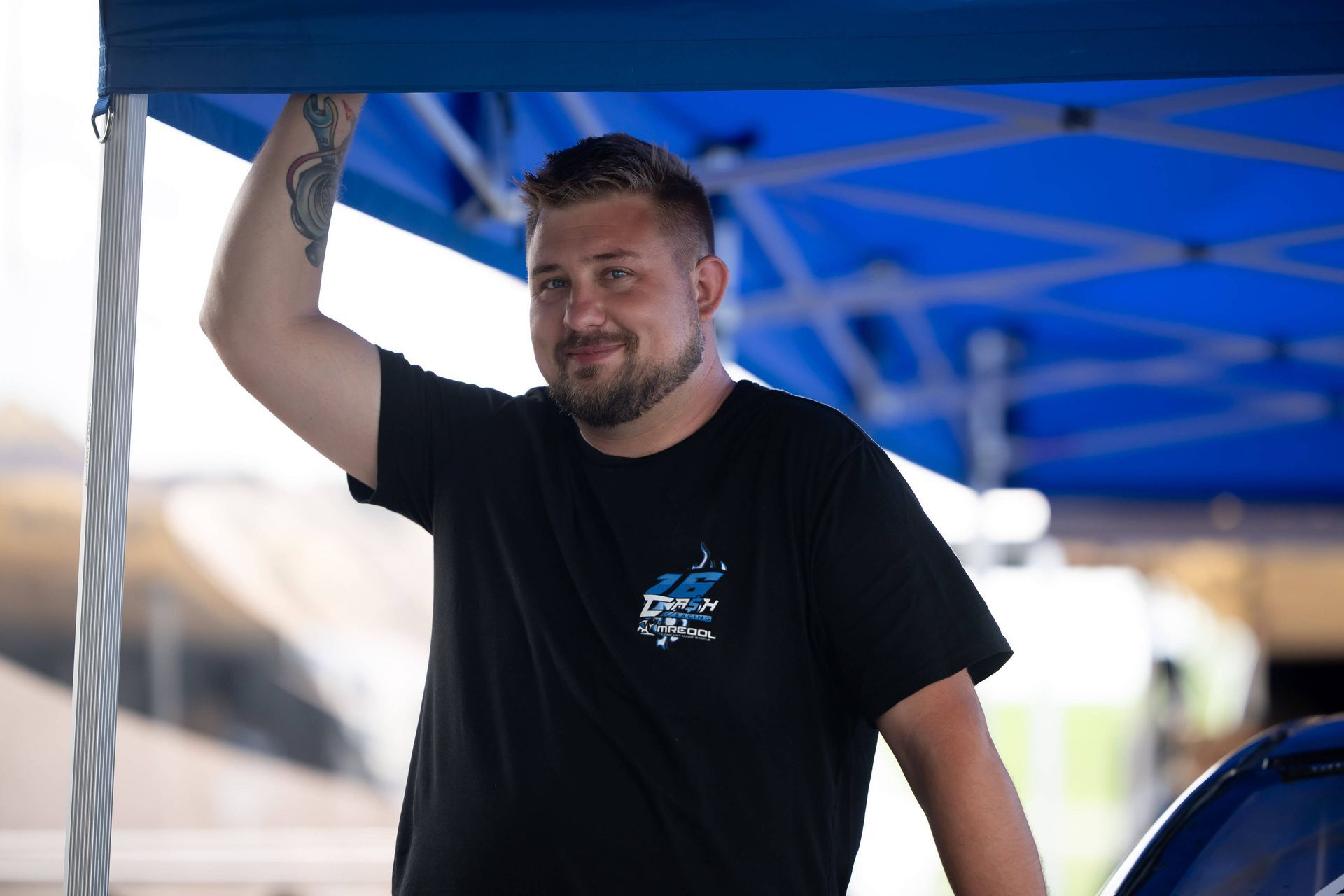 A man with a tattoo on his arm is standing under a blue tent.