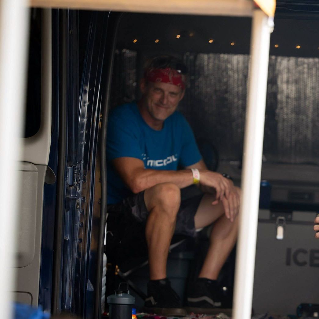 A man wearing a blue shirt that says mcpol sits in a dark room