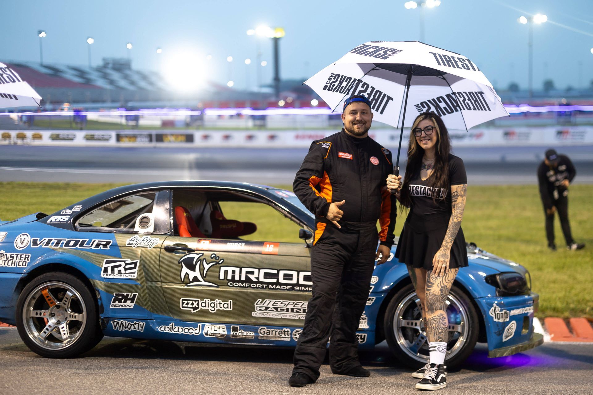 A man and a woman are standing next to a race car on a track.