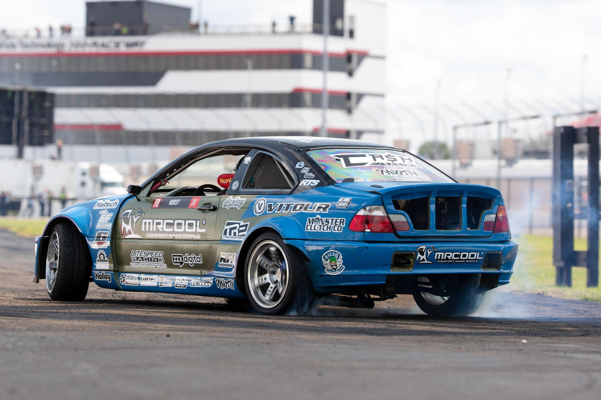 The Cash Racing Mr. Cool BMW blue race car is drifting on a race track.