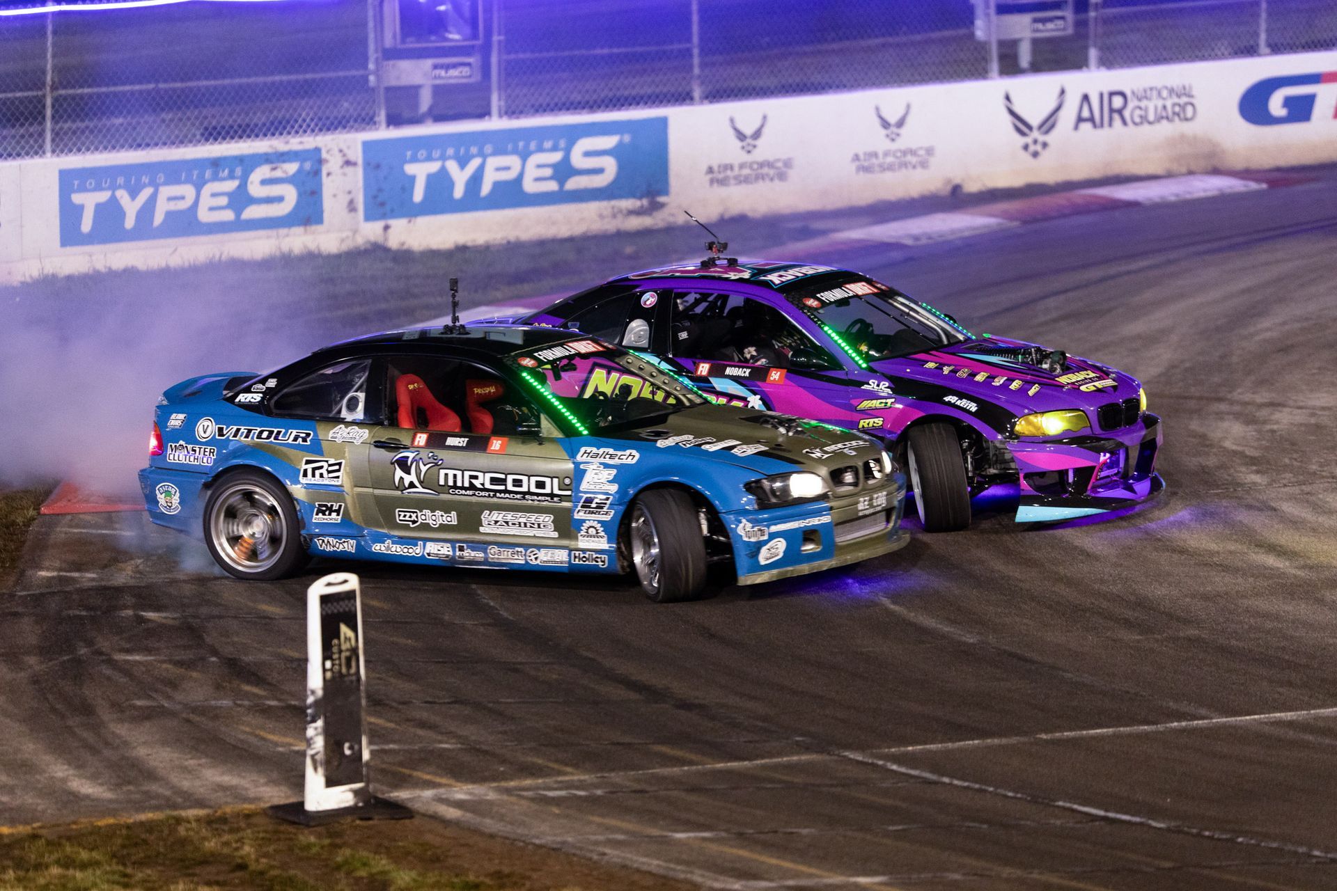 Two cars are racing on a track with a sign that says types