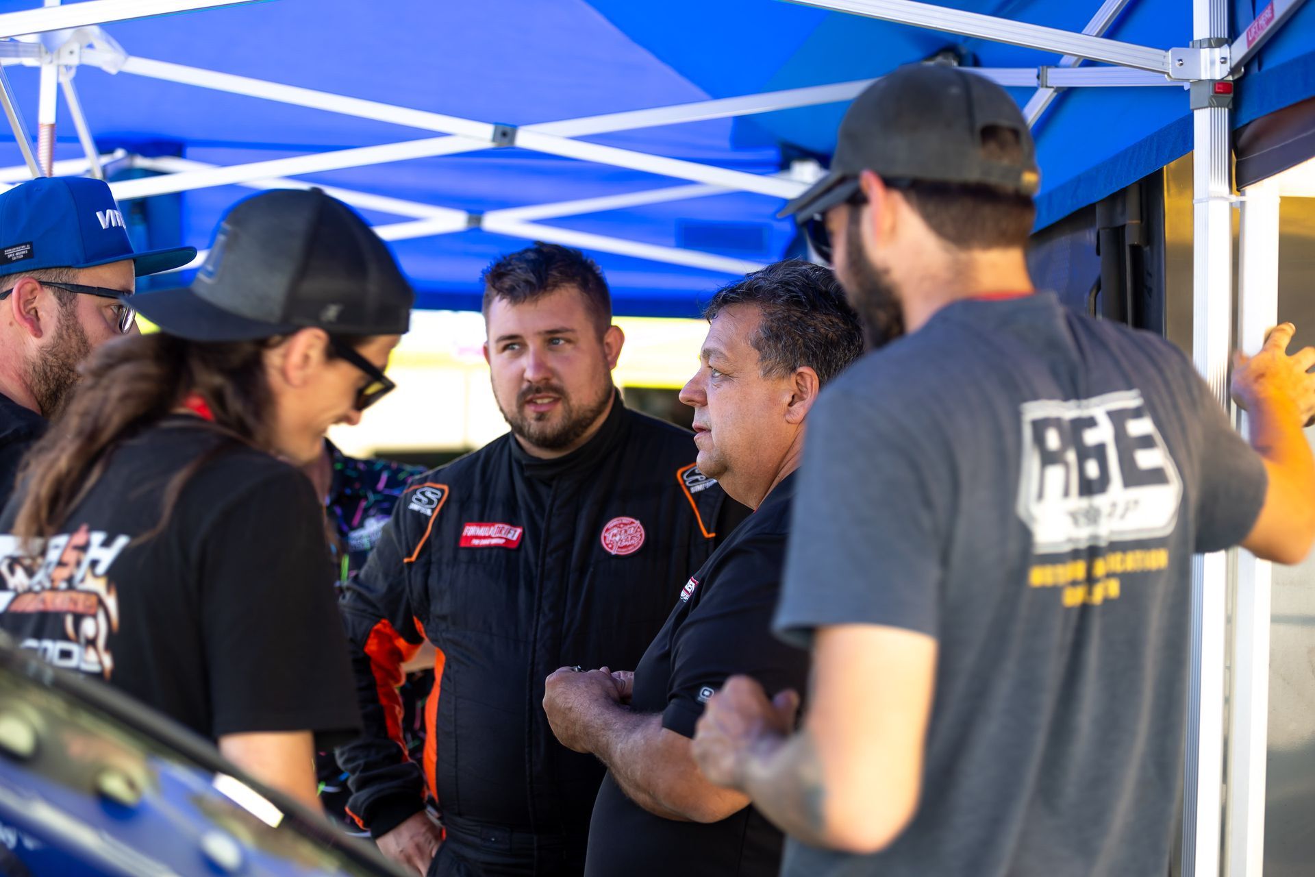 A group of men on cash racing race team are standing under a blue tent talking to each other.