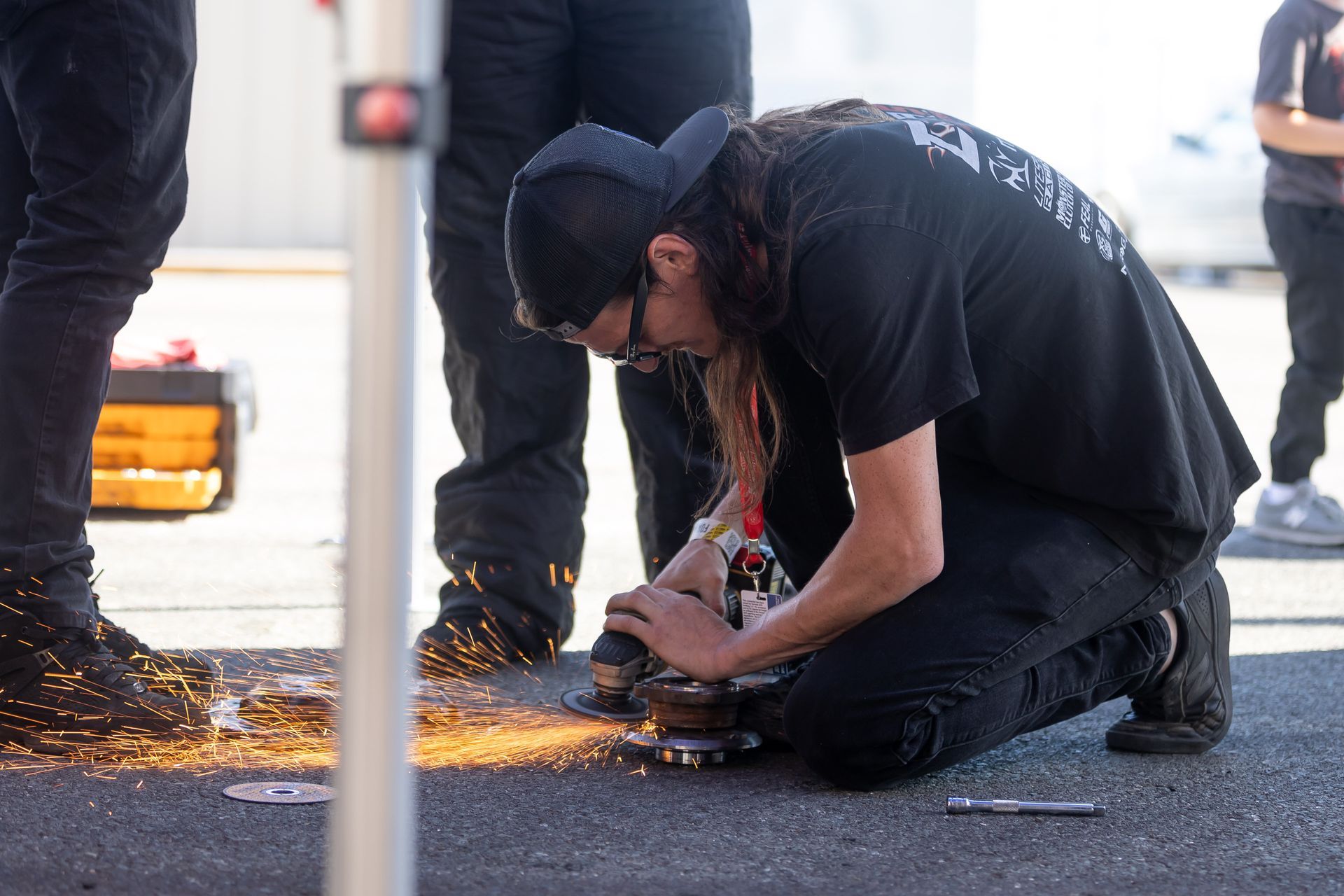 A man is kneeling down on the ground working on a piece of metal.