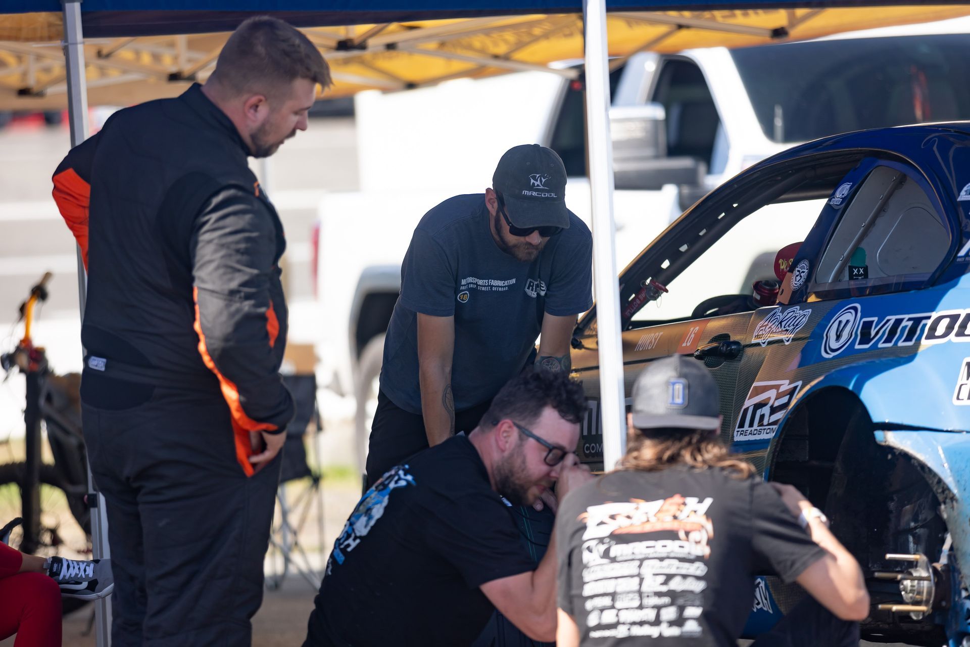 A group of men on the Cash Racing Team are working on a race car under a tent.