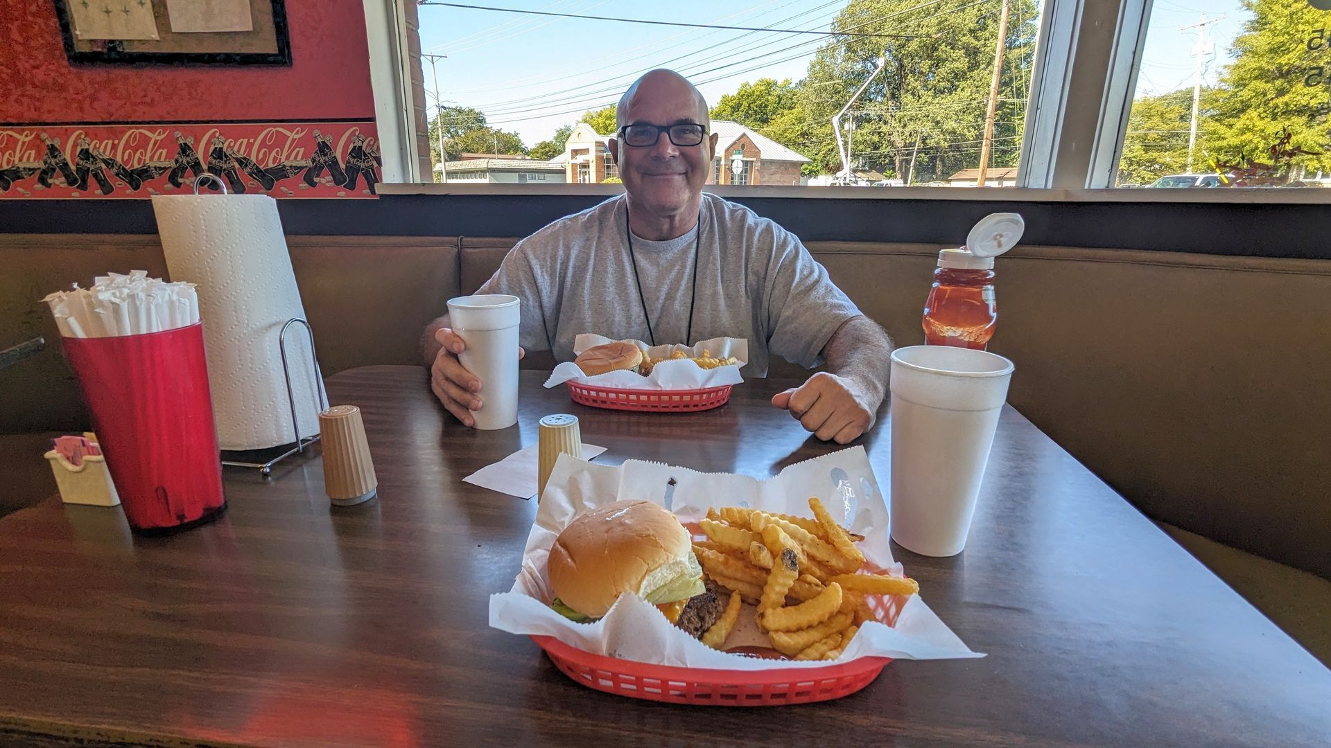 A man is sitting at a table with a hamburger and french fries.