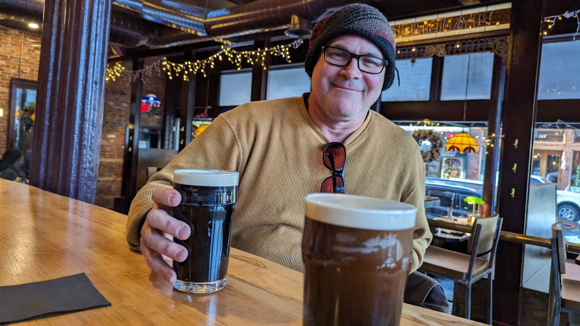 A man is sitting at a bar holding two glasses of beer.