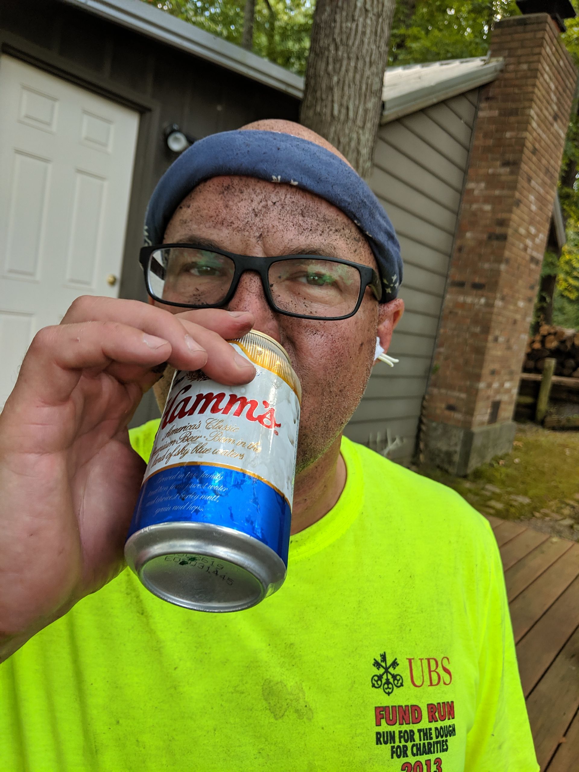 A man wearing glasses is drinking from a can of beer.