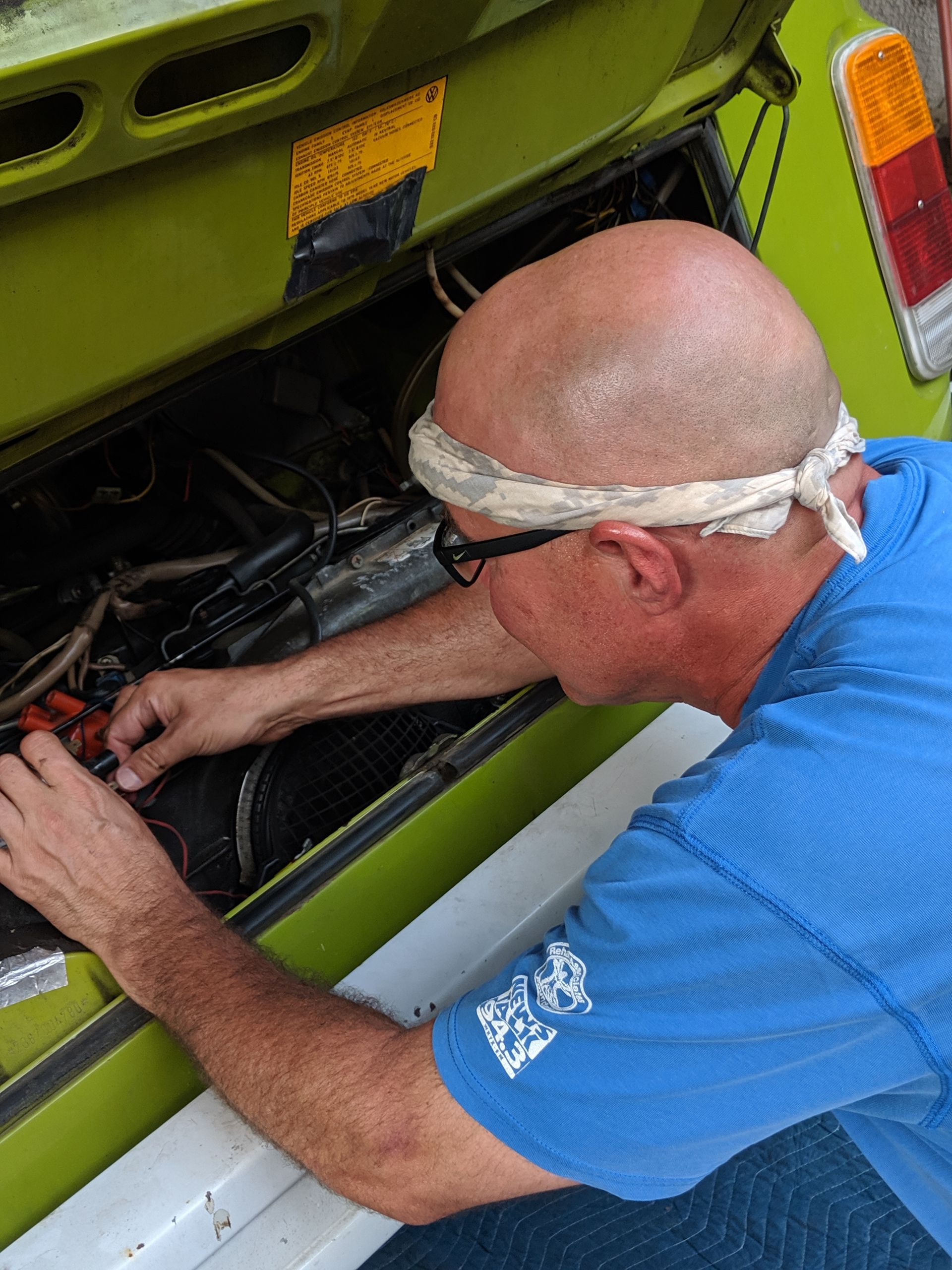 A man in a blue shirt is working on the engine of a green car.