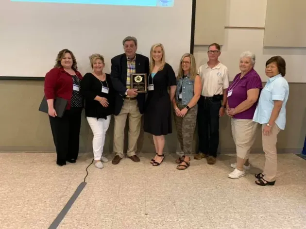 People in a conference room having a discussion, some looking at documents on tables.