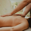 A massage therapist in a black uniform massages a client’s shoulders in a room with text on the wall.