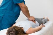 A practitioner performs a back adjustment on a person lying prone on a treatment table.
