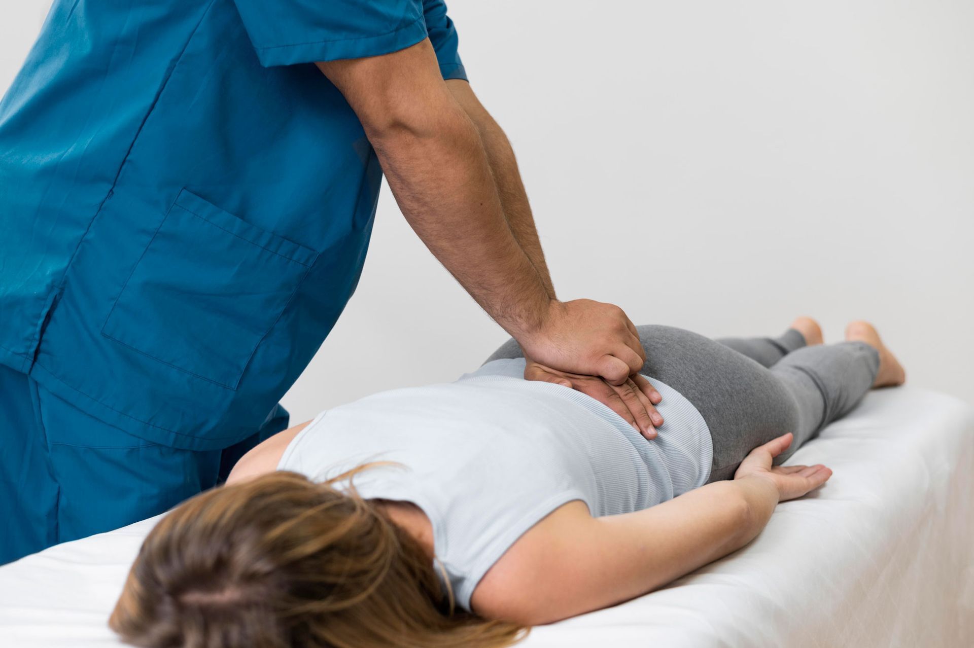 A practitioner performs a back adjustment on a person lying prone on a treatment table.