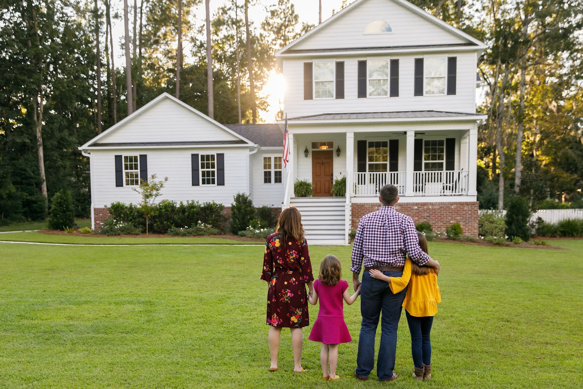 A family is standing in front of a large white house.