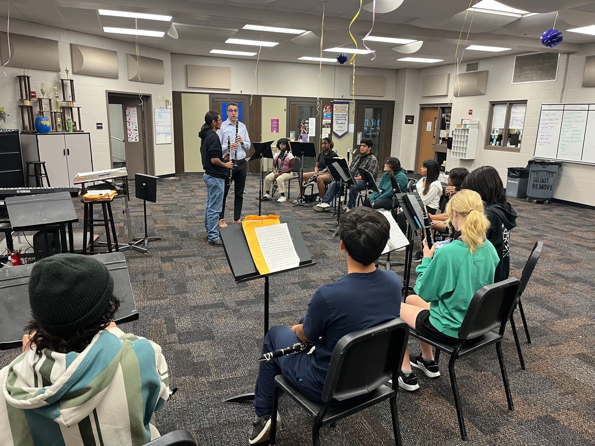 Oscar Ruiz-Espina with student demonstrating woodwind instrument in a classroom. Students seated, some with music stands.
