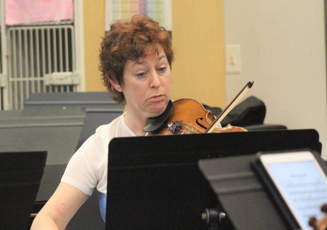 Jennifer Leshnower playing a violin in an orchestra, holding instrument, looking at sheet music.