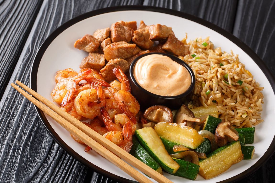 Japanese Hibachi recipe of rice, shrimp, steak and vegetables served with sauce closeup in a plate.