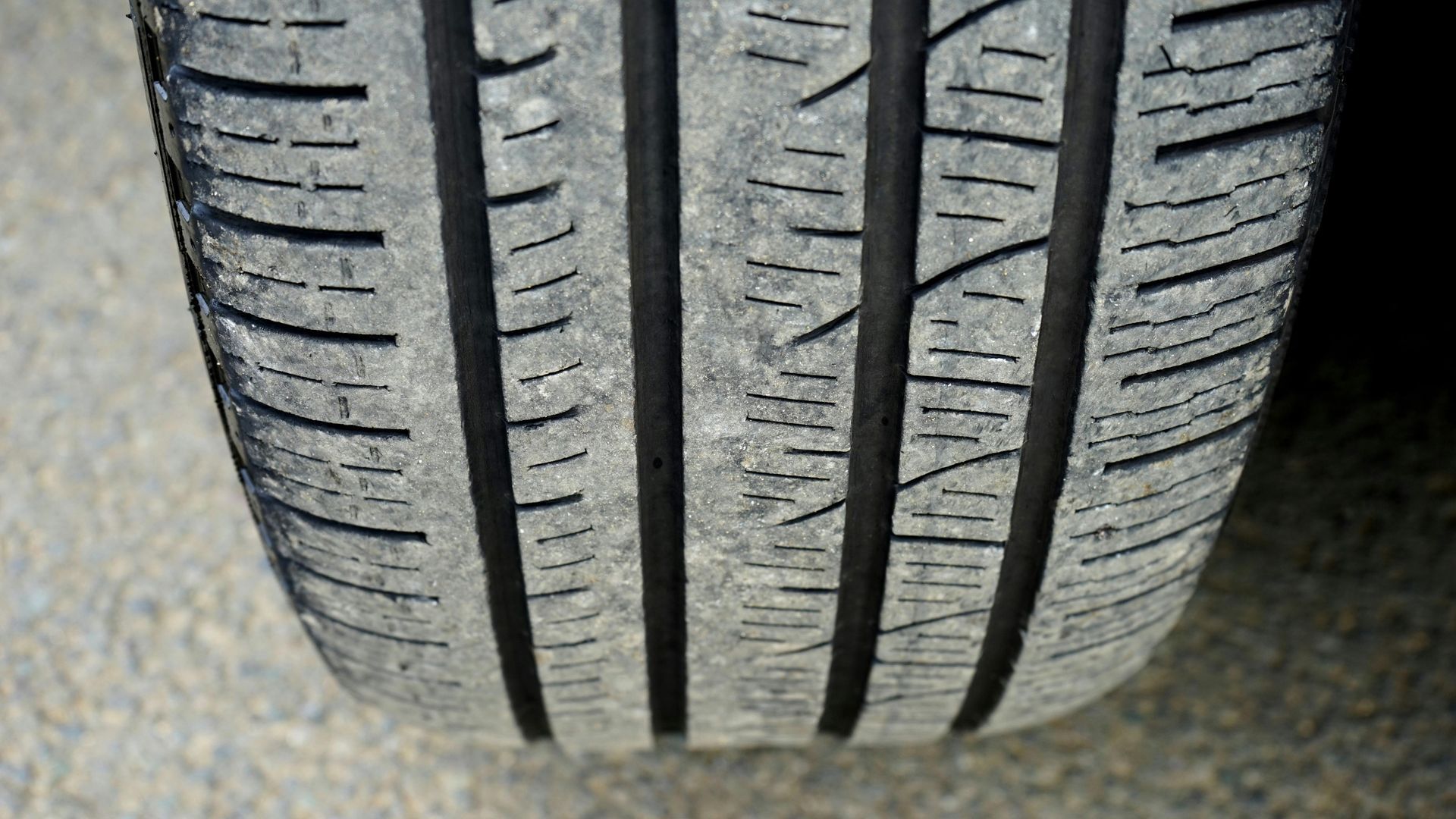 Close-up of a car tire tread. Black rubber with visible wear, deep grooves, and small cracks.
