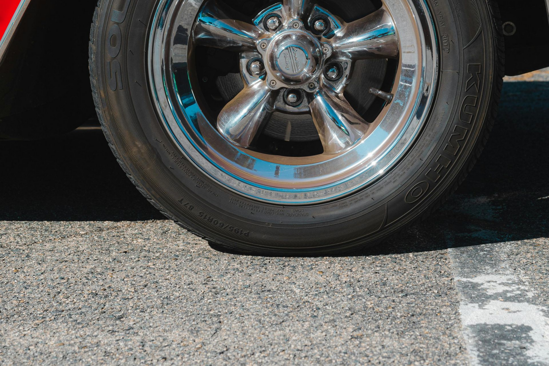Close-up of a car's chrome rim and black tire on asphalt, light reflecting.