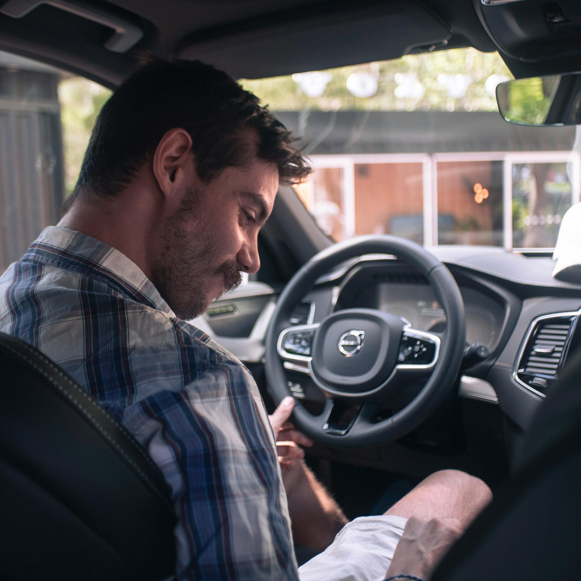 Man sitting in Volvo, looking down, holding the steering wheel. Inside of the car, natural light.