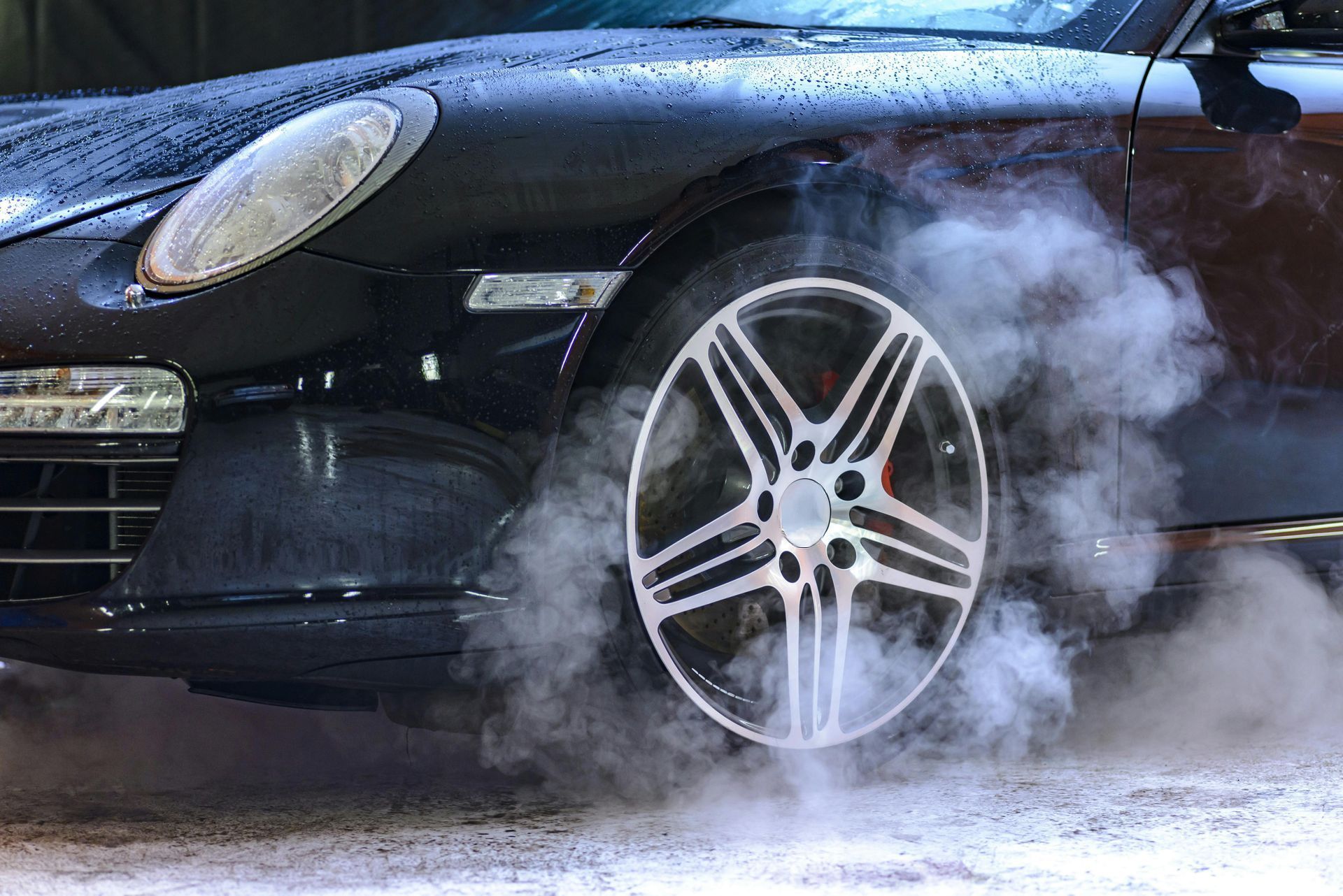 Black sports car doing a burnout, smoke rising from the tires.