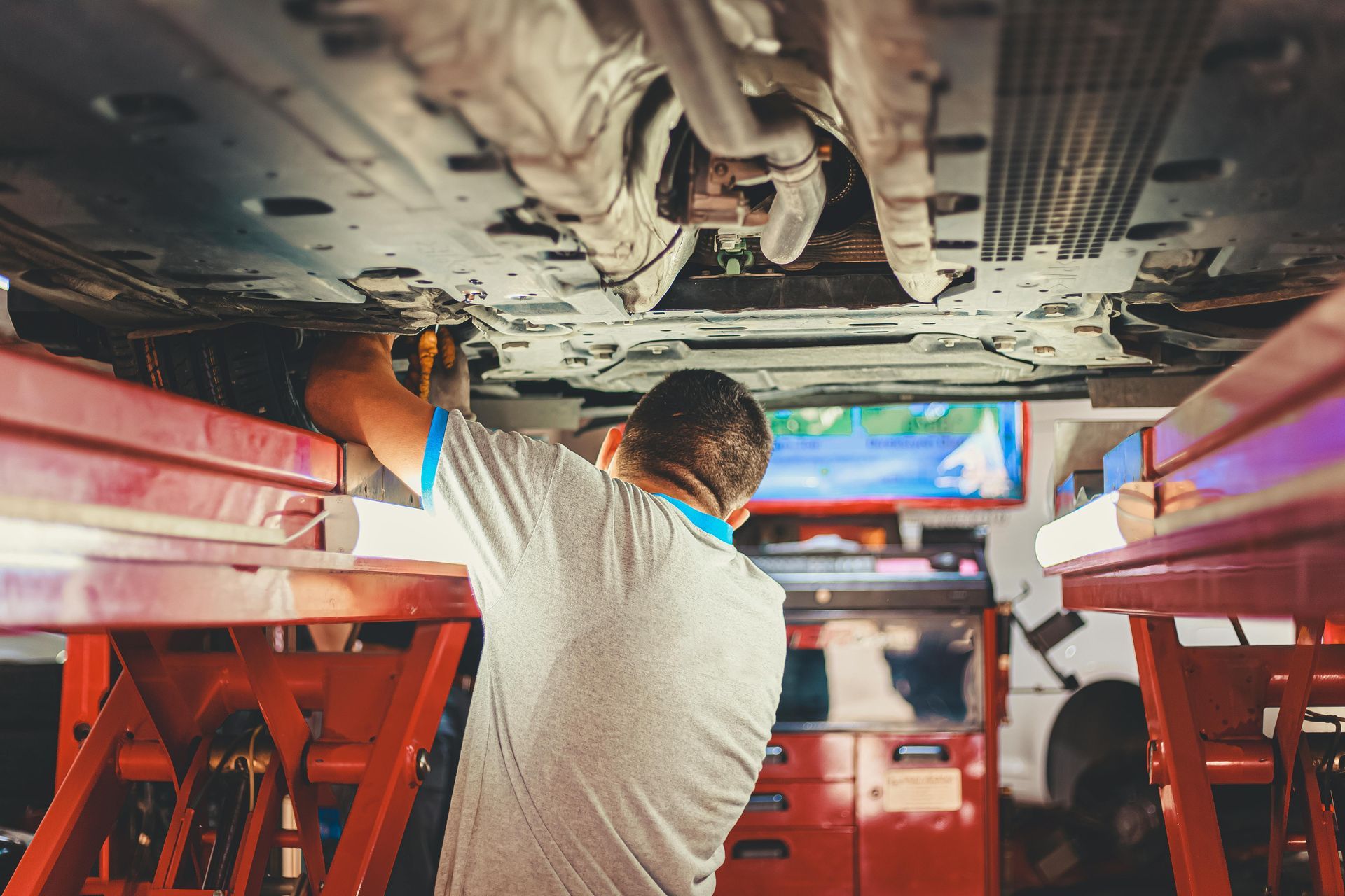 Mechanic working under a car on a lift in a garage, using a tool.