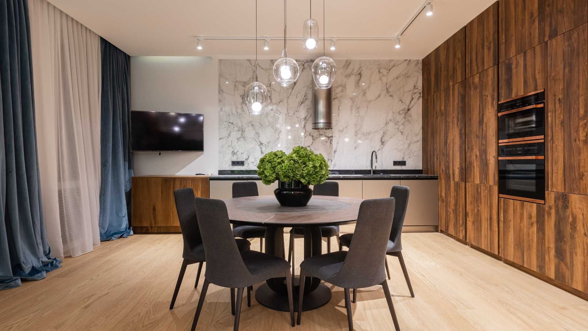 A dining room with a round table and chairs and a television.