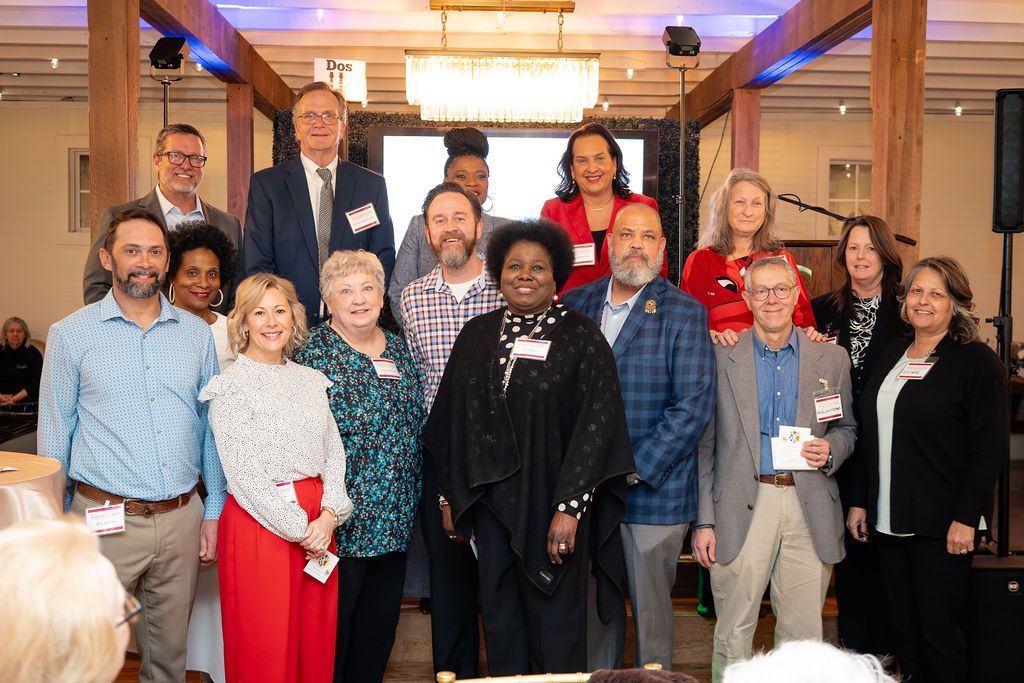 Group of people posing for a photo indoors, some holding items, under bright lights.